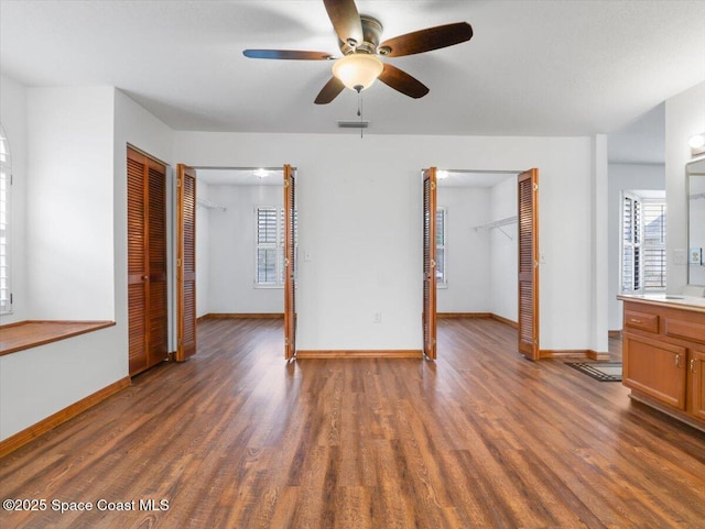 unfurnished bedroom with a closet, a spacious closet, dark hardwood / wood-style floors, and ceiling fan