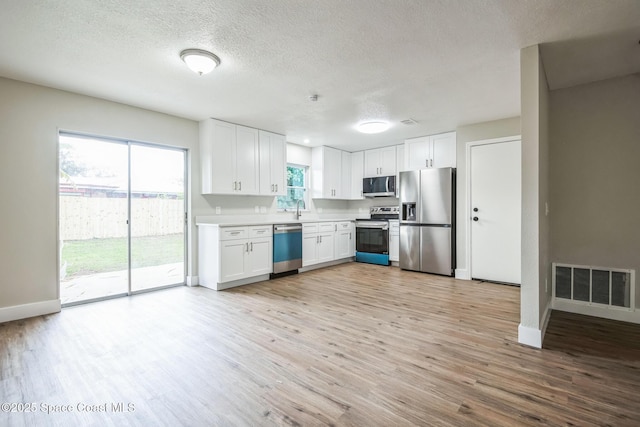 kitchen featuring white cabinetry, light wood-type flooring, a textured ceiling, and appliances with stainless steel finishes