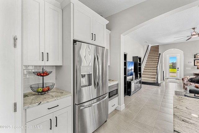 kitchen featuring ceiling fan, appliances with stainless steel finishes, white cabinetry, light stone counters, and decorative backsplash