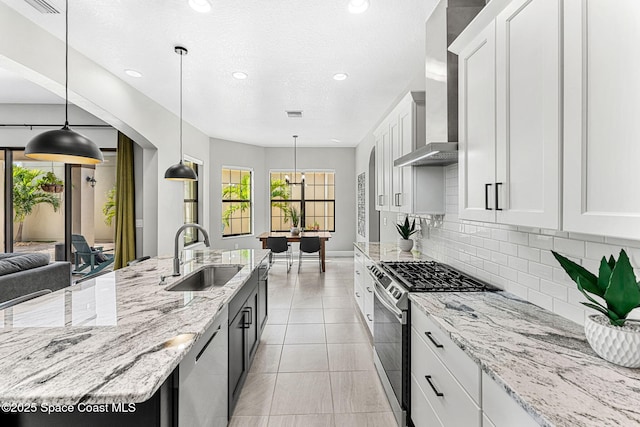 kitchen with sink, hanging light fixtures, appliances with stainless steel finishes, white cabinets, and wall chimney range hood