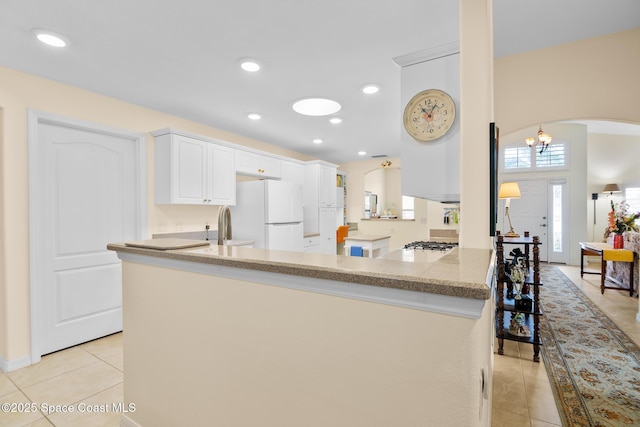 kitchen with white cabinetry, white fridge, light tile patterned floors, and kitchen peninsula