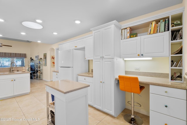 kitchen featuring built in desk, white cabinetry, sink, white refrigerator, and light tile patterned floors