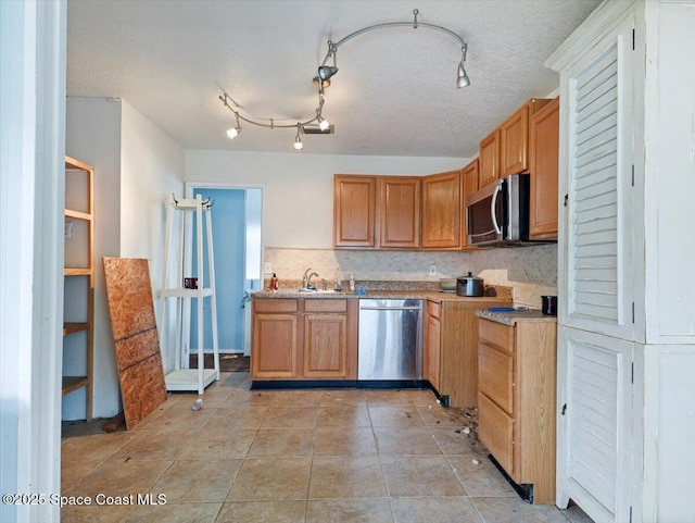 kitchen with sink, a textured ceiling, light tile patterned floors, appliances with stainless steel finishes, and decorative backsplash