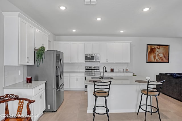 kitchen featuring a breakfast bar, white cabinetry, stainless steel appliances, a kitchen island with sink, and backsplash