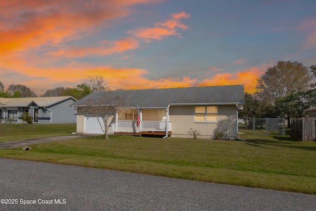 view of front facade with aphalt driveway, covered porch, an attached garage, a front yard, and fence