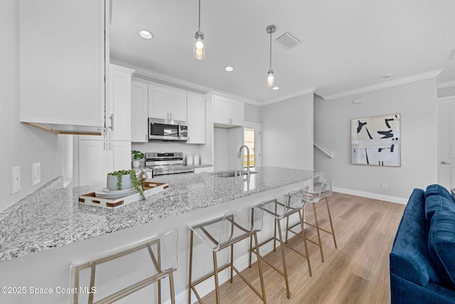 kitchen featuring sink, a breakfast bar, stainless steel appliances, white cabinets, and decorative light fixtures