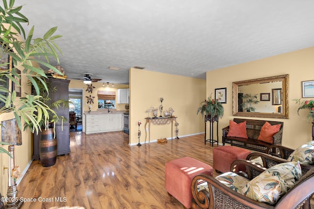 living room featuring ceiling fan, a textured ceiling, and light wood-type flooring