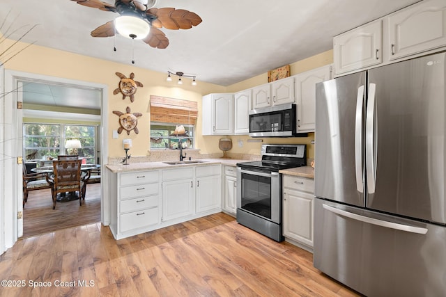 kitchen featuring sink, appliances with stainless steel finishes, light stone countertops, light hardwood / wood-style floors, and white cabinets