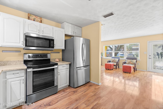 kitchen featuring a textured ceiling, light wood-type flooring, white cabinets, and appliances with stainless steel finishes