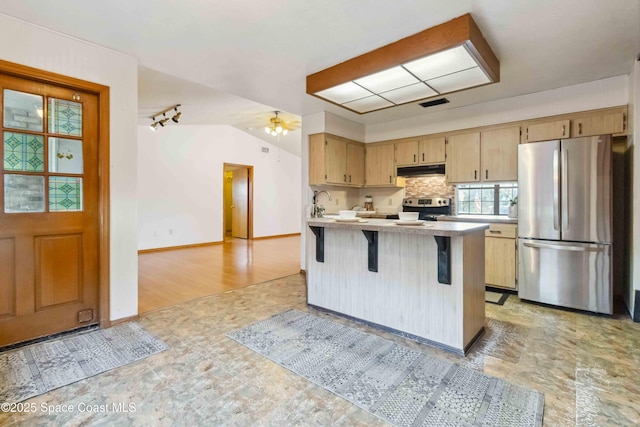 kitchen featuring lofted ceiling, a breakfast bar, stainless steel appliances, light brown cabinetry, and kitchen peninsula