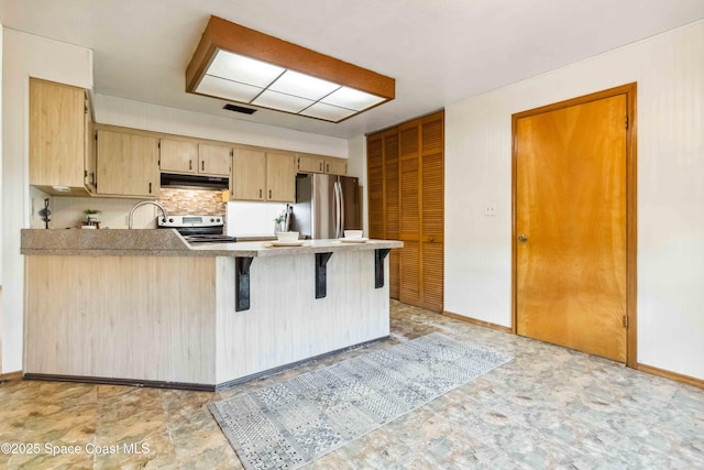 kitchen with a breakfast bar area, appliances with stainless steel finishes, decorative backsplash, kitchen peninsula, and light brown cabinets