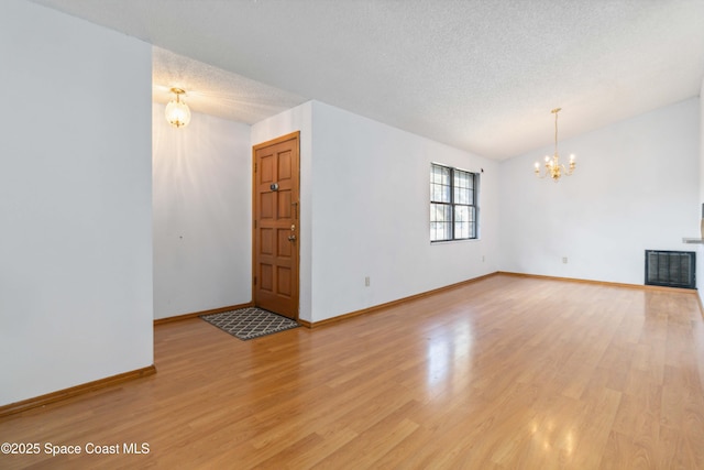 unfurnished living room with an inviting chandelier, light hardwood / wood-style floors, and a textured ceiling