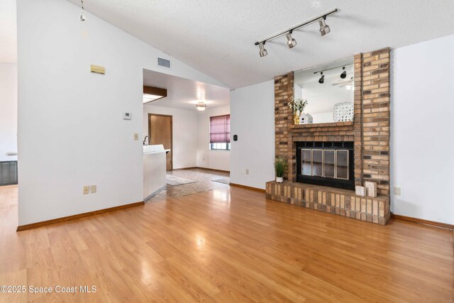 unfurnished living room featuring light hardwood / wood-style flooring, a brick fireplace, vaulted ceiling, and a textured ceiling