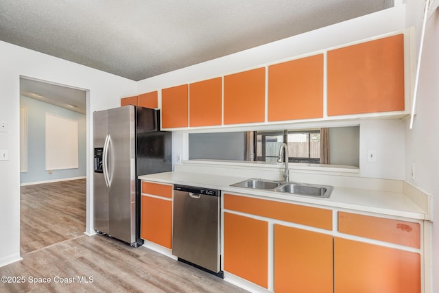 kitchen with a textured ceiling, a sink, light wood-style floors, light countertops, and appliances with stainless steel finishes