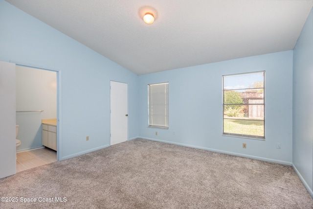 unfurnished bedroom with lofted ceiling, baseboards, connected bathroom, and light colored carpet