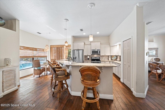 kitchen with appliances with stainless steel finishes, white cabinets, a kitchen breakfast bar, hanging light fixtures, and a kitchen island with sink