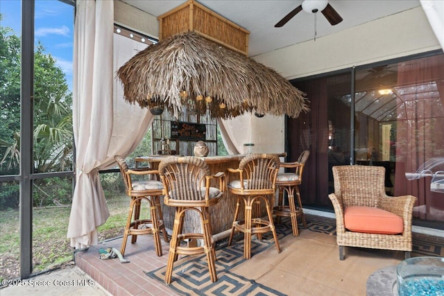 sunroom / solarium featuring a healthy amount of sunlight, bar area, and ceiling fan