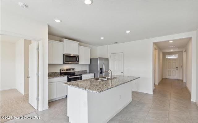 kitchen featuring light stone countertops, white cabinetry, appliances with stainless steel finishes, and an island with sink