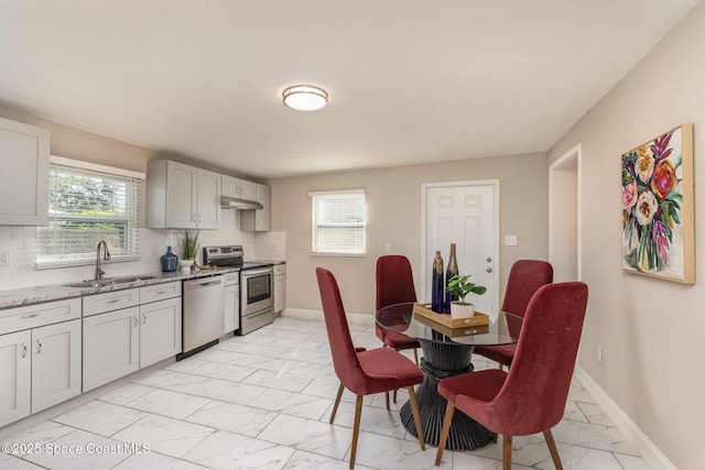 kitchen featuring baseboards, under cabinet range hood, marble finish floor, stainless steel appliances, and a sink