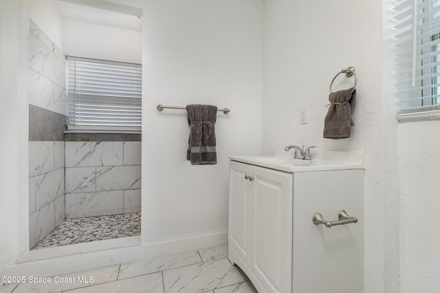 bathroom featuring vanity, baseboards, marble finish floor, and a tile shower