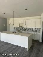 kitchen with pendant lighting, white cabinetry, and a kitchen island with sink