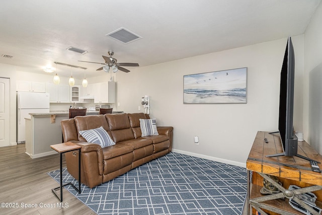 living area with visible vents, ceiling fan, baseboards, and wood finished floors