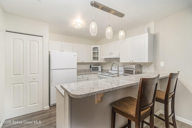 kitchen featuring a breakfast bar area, under cabinet range hood, a peninsula, white appliances, and glass insert cabinets