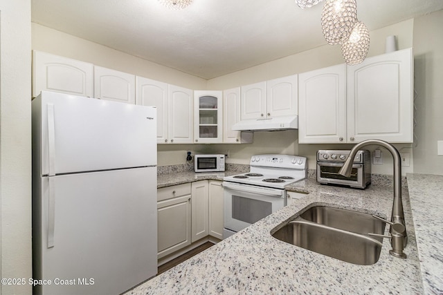 kitchen with light stone counters, under cabinet range hood, white appliances, a sink, and white cabinetry