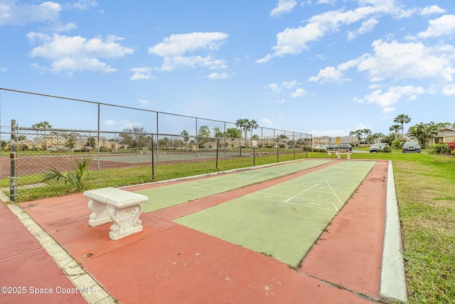 view of property's community with fence, a lawn, and shuffleboard