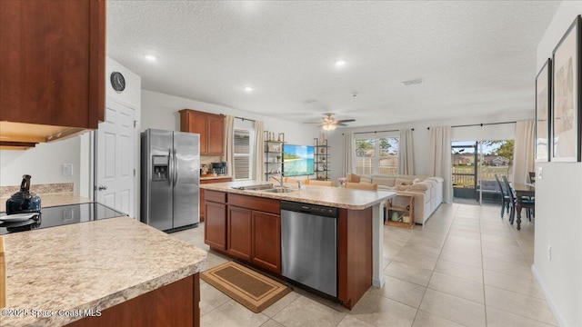 kitchen featuring appliances with stainless steel finishes, an island with sink, sink, ceiling fan, and a textured ceiling