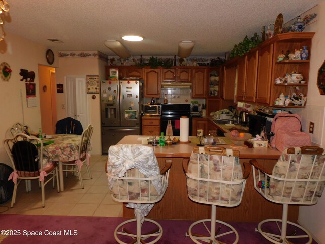 kitchen with stove, light tile patterned floors, a textured ceiling, and stainless steel refrigerator with ice dispenser