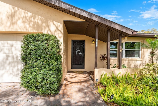 view of exterior entry with an attached garage and stucco siding