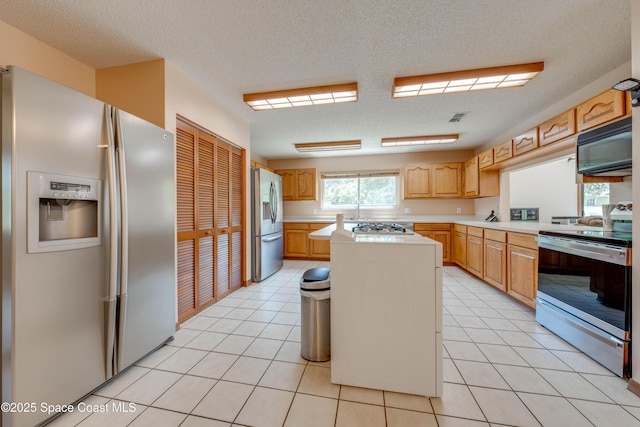 kitchen with sink, a textured ceiling, light tile patterned floors, appliances with stainless steel finishes, and a kitchen island