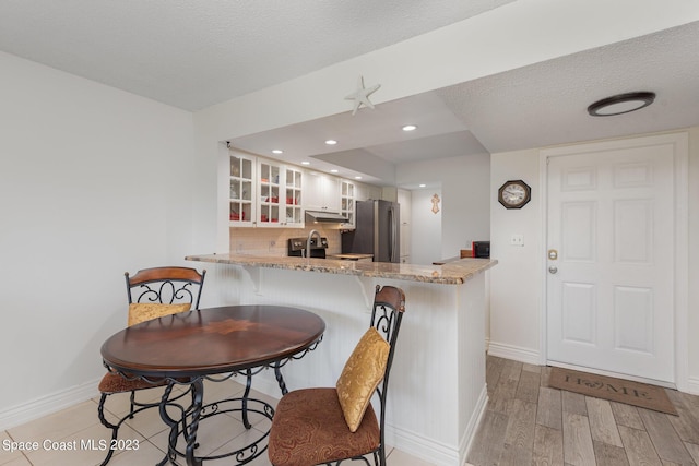 kitchen with light hardwood / wood-style flooring, white cabinets, decorative backsplash, stainless steel refrigerator, and kitchen peninsula