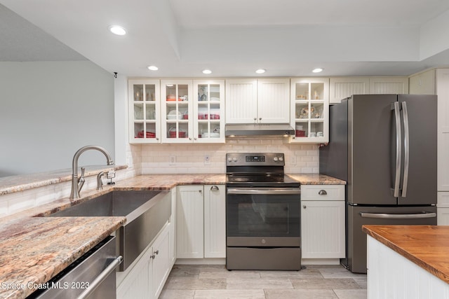 kitchen with light stone countertops, sink, backsplash, appliances with stainless steel finishes, and white cabinets