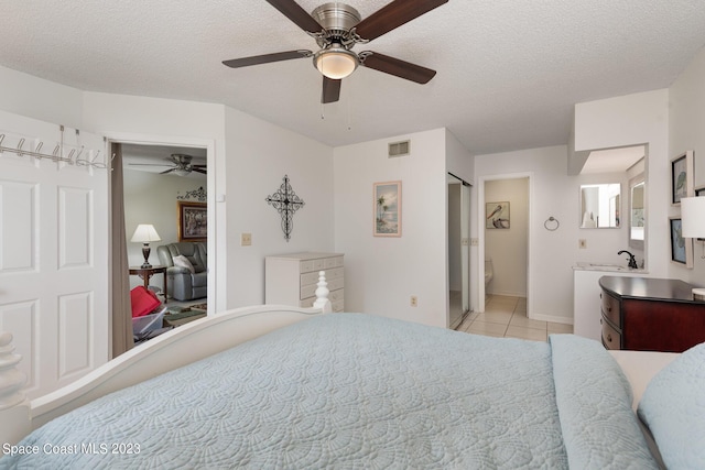 bedroom featuring light tile patterned flooring, ensuite bathroom, ceiling fan, and a textured ceiling