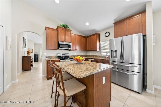 kitchen with sink, a center island, light tile patterned floors, stainless steel appliances, and light stone countertops