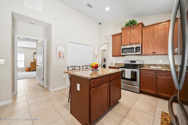 kitchen featuring light stone counters, appliances with stainless steel finishes, a center island, and light tile patterned floors