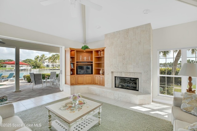 living room with a water view, lofted ceiling with beams, light tile patterned floors, ceiling fan, and a fireplace