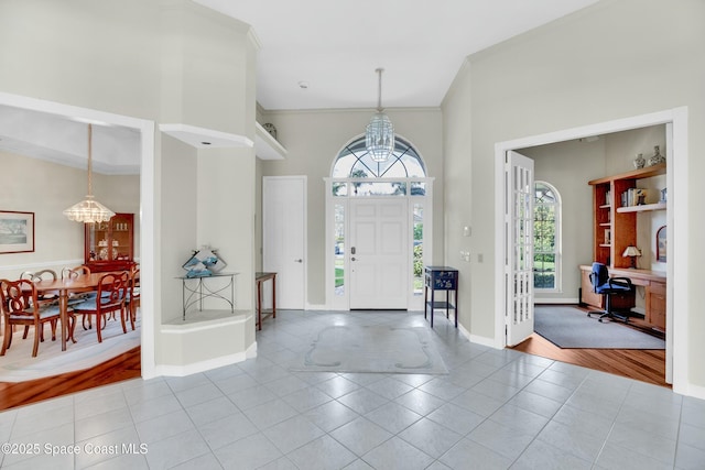 tiled foyer entrance with a high ceiling, ornamental molding, and an inviting chandelier