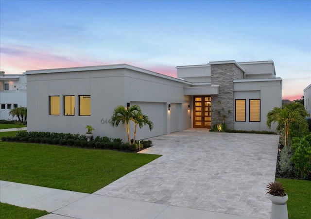 contemporary home featuring stucco siding, concrete driveway, a garage, stone siding, and a front lawn