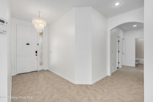 foyer featuring baseboards, arched walkways, an inviting chandelier, a textured ceiling, and light tile patterned flooring