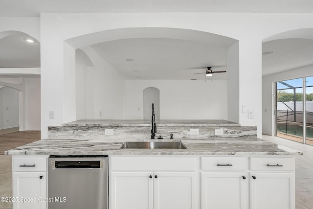 kitchen with ceiling fan, light stone countertops, stainless steel dishwasher, white cabinetry, and a sink