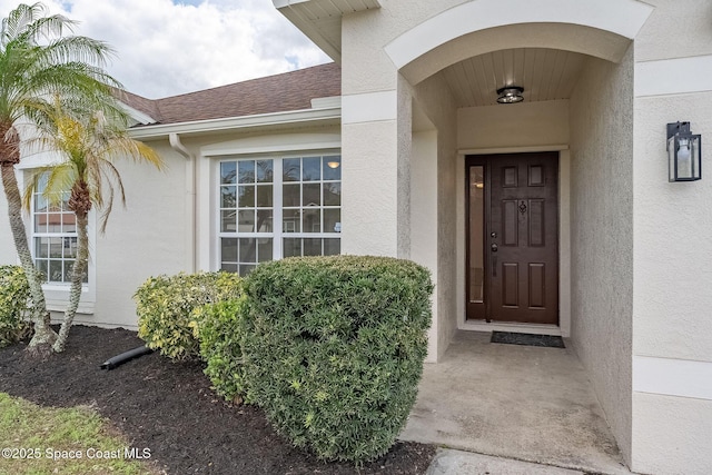 view of exterior entry with a shingled roof and stucco siding