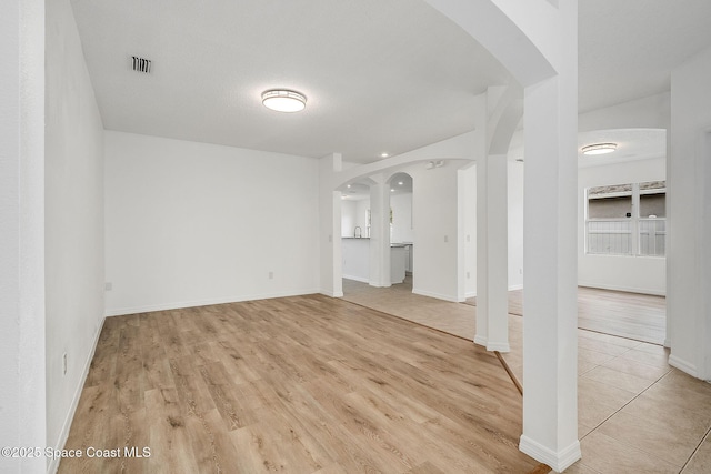 spare room featuring arched walkways, visible vents, light wood-style flooring, and baseboards