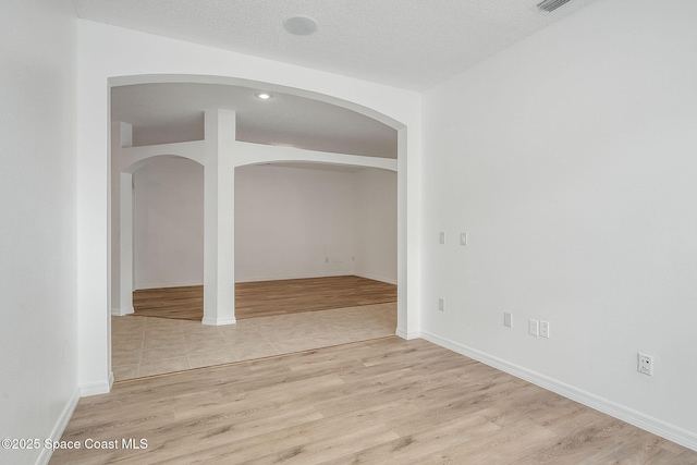 spare room featuring light wood-type flooring, baseboards, and a textured ceiling