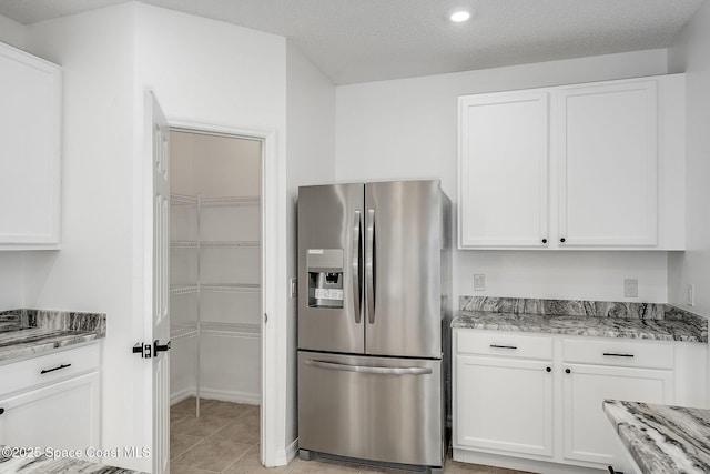 kitchen featuring light stone countertops, stainless steel fridge, light tile patterned floors, and white cabinetry