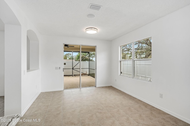 tiled empty room featuring baseboards, visible vents, and a textured ceiling