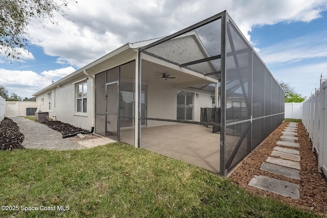 back of property with a yard, a patio, stucco siding, glass enclosure, and a fenced backyard