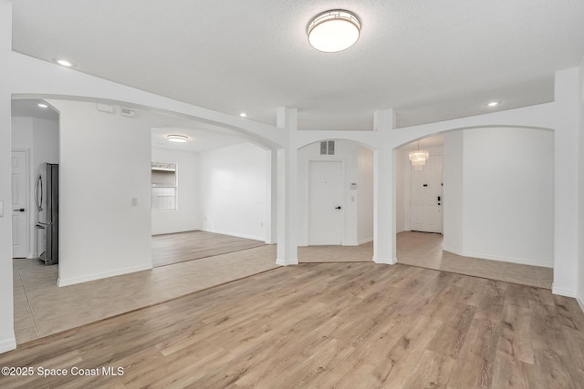 spare room featuring arched walkways, visible vents, light wood-style flooring, and recessed lighting